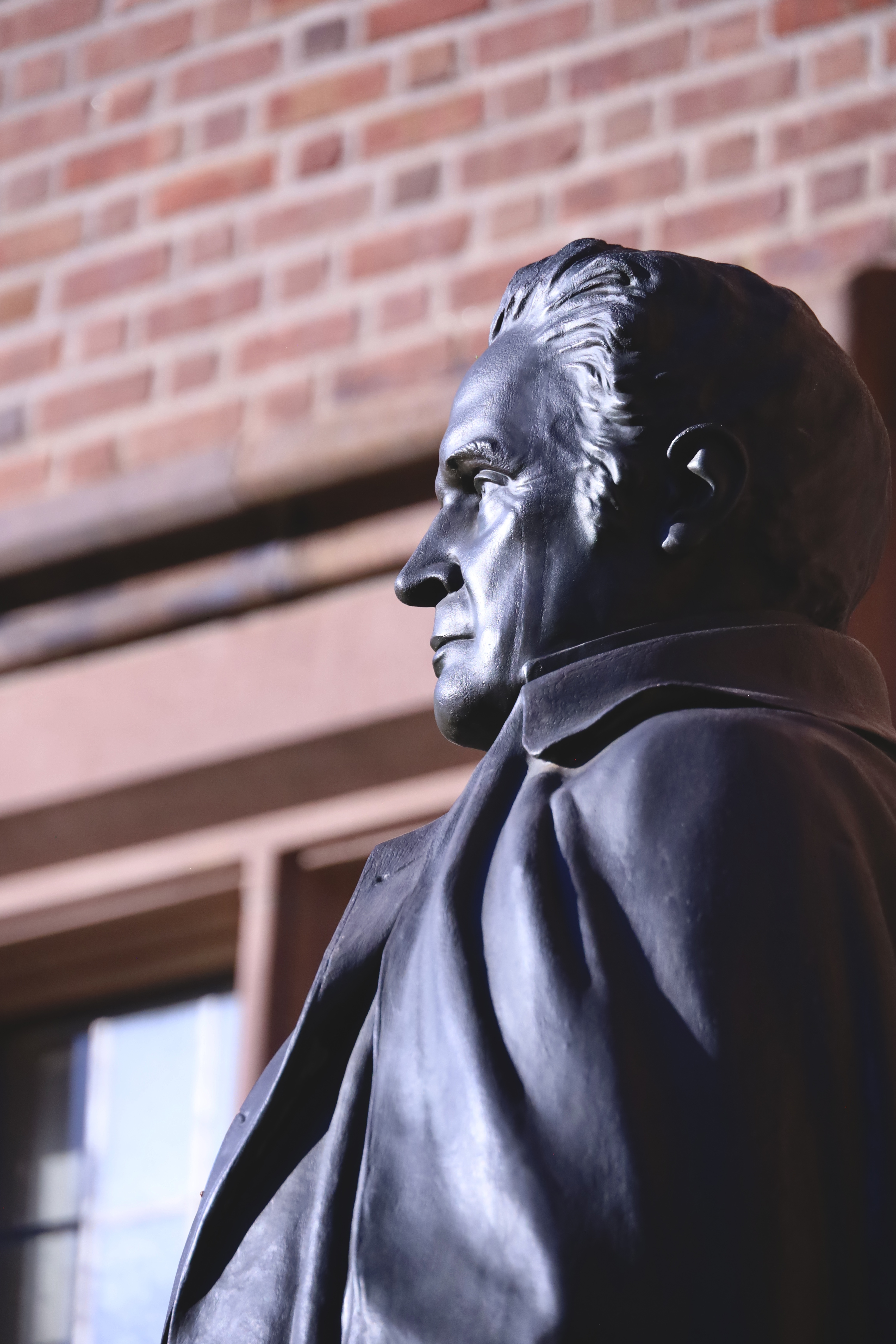 Metal bust of a historical figure against brick wall