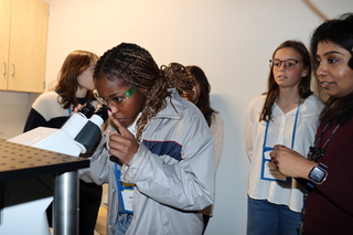 Girl looking into microscope while other girls watch