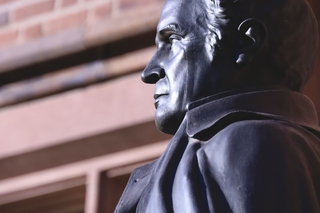 Metal bust of a historical figure against brick wall