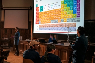 man looking at giant periodic table on monitor