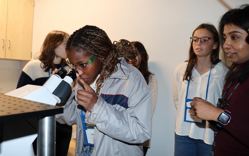 Girl looking into microscope while other girls watch