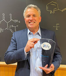 Man holding glass award in front of chalk board