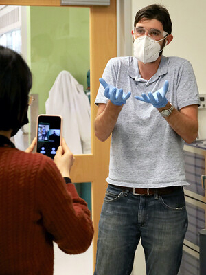 man in mask and gloves gesturing to a phone