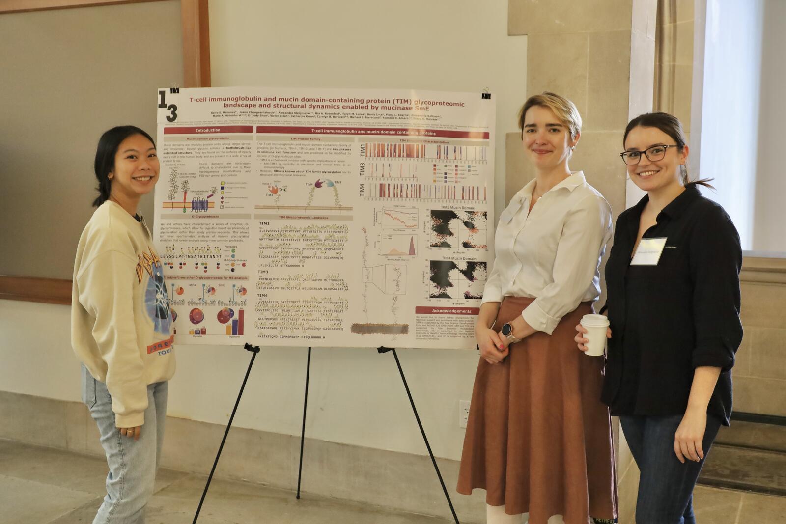 Three women posing near research poster