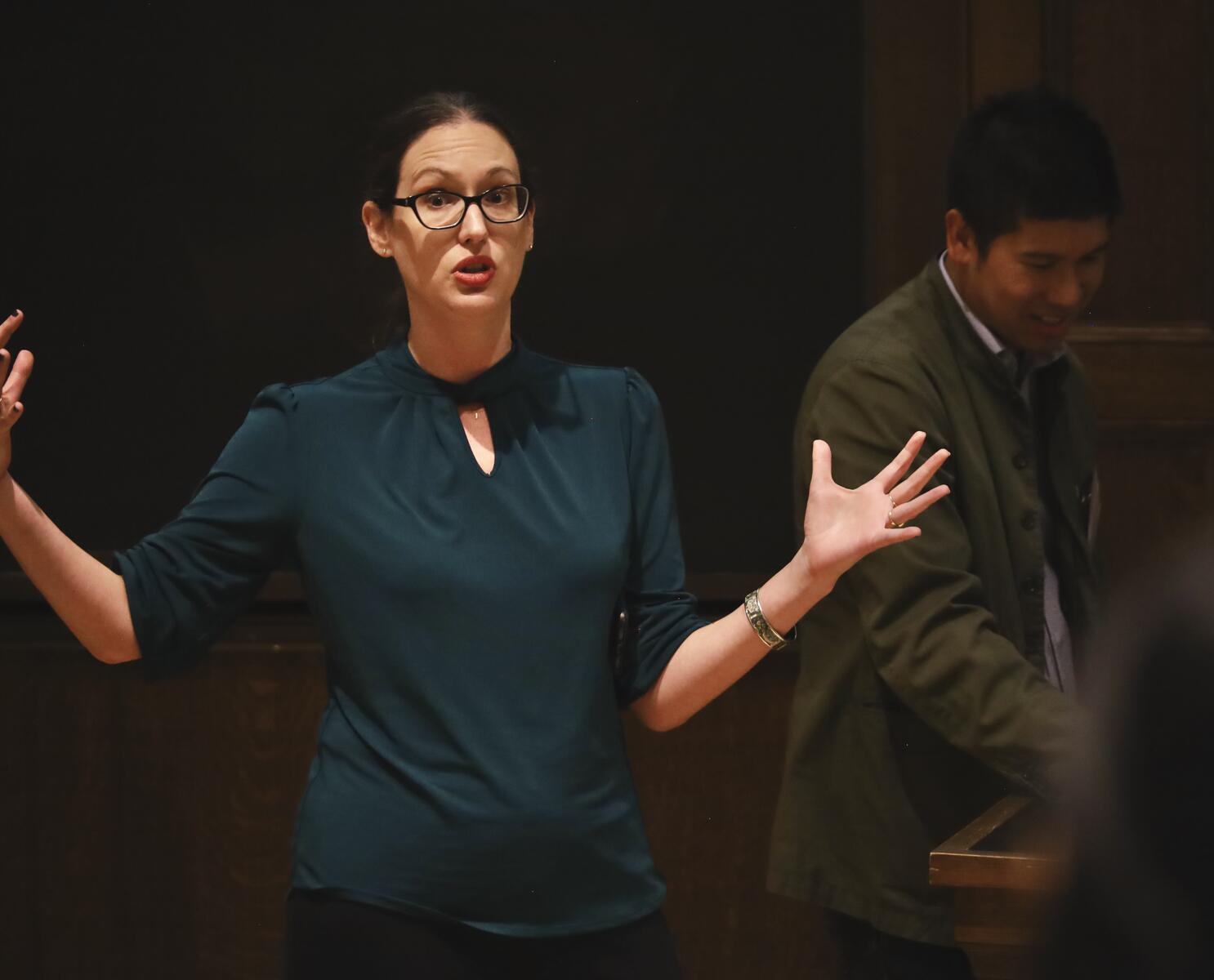 Woman pointing and gesturing in front of blackboard